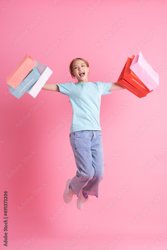 Young Asian woman holding shopping bag on pink background