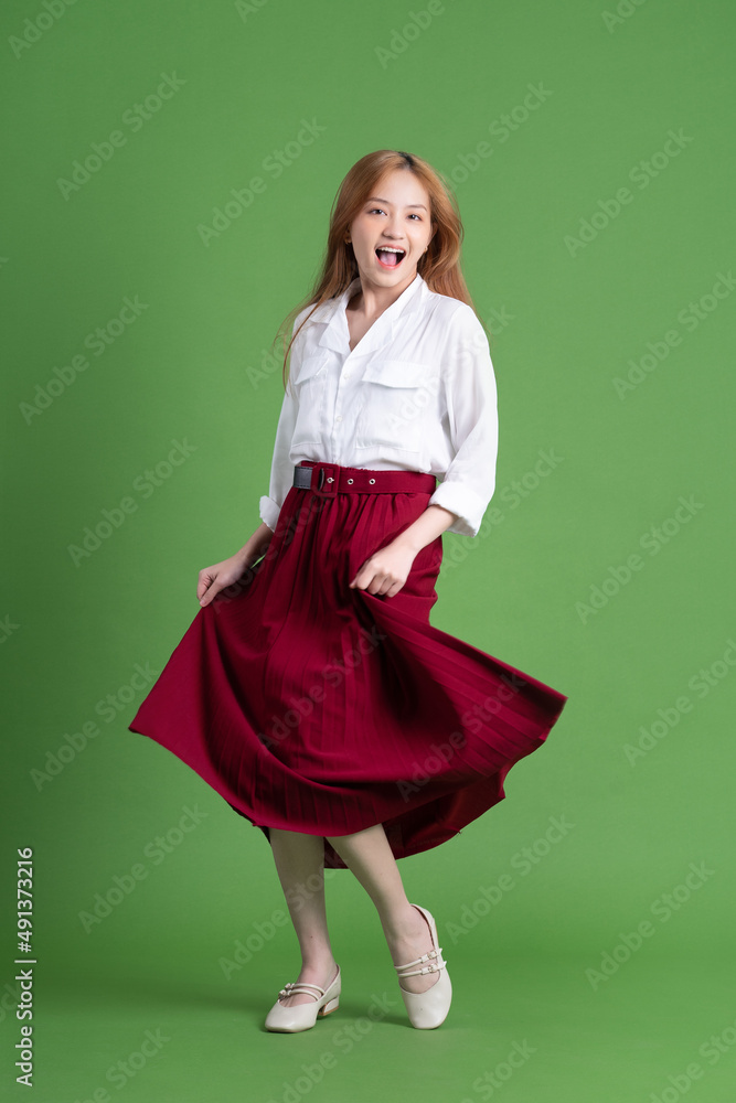 Beautiful young Asian woman dancing and posing on green background