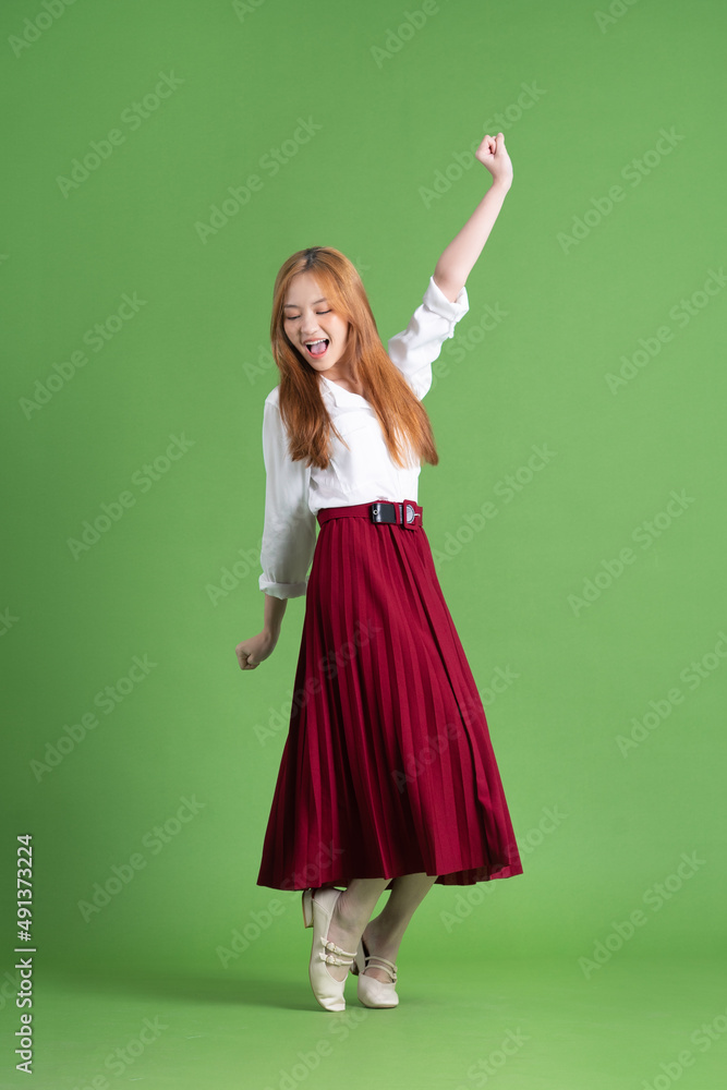 Beautiful young Asian woman dancing and posing on green background