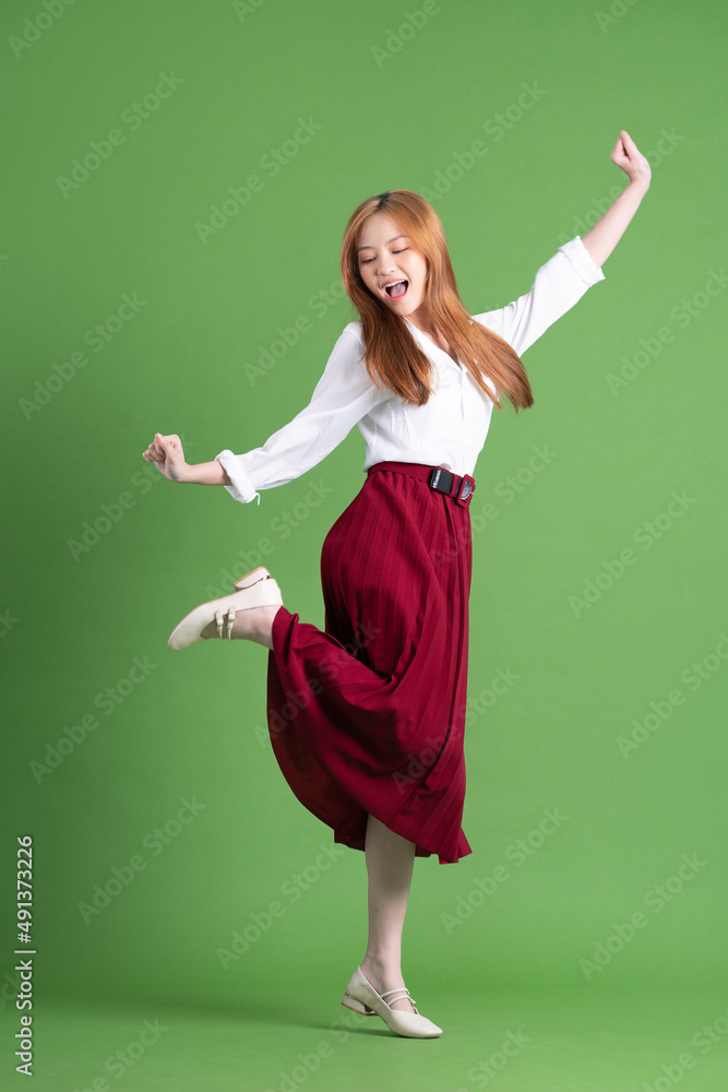 Beautiful young Asian woman dancing and posing on green background