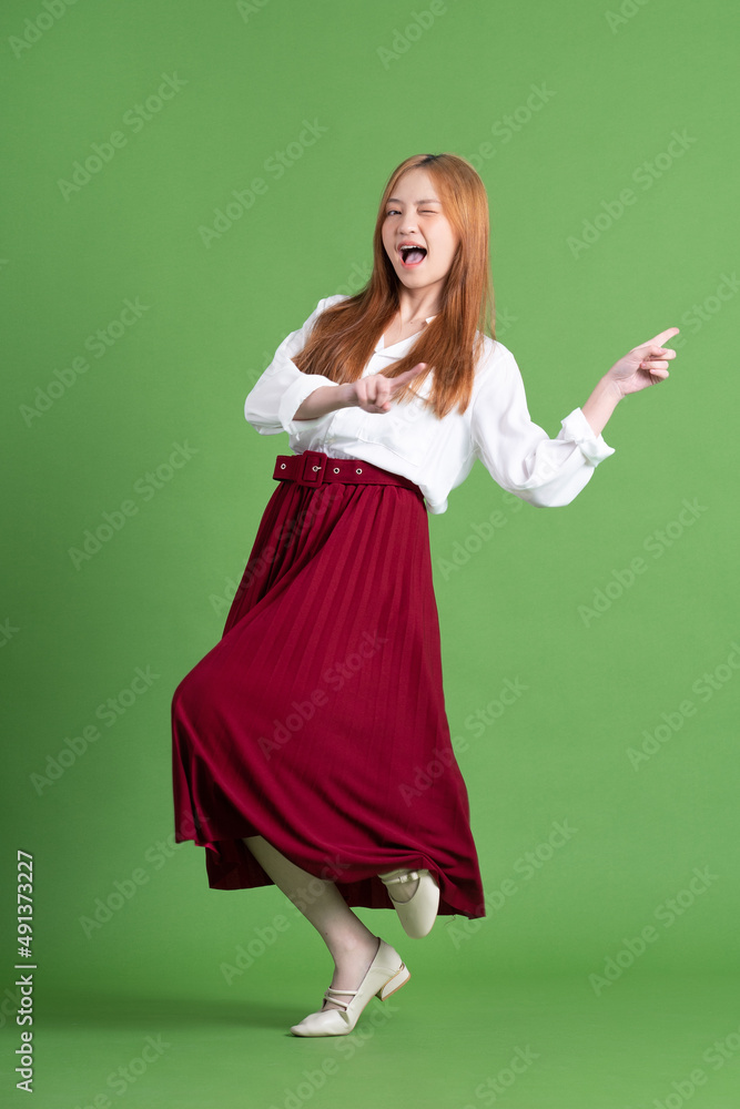 Beautiful young Asian woman dancing and posing on green background