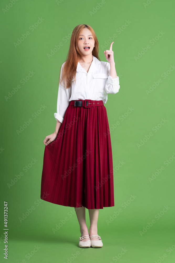 Beautiful young Asian woman dancing and posing on green background