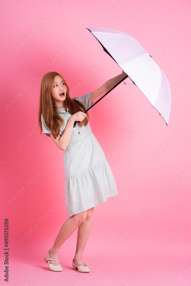 Young Asian woman holding umbrella on pink background