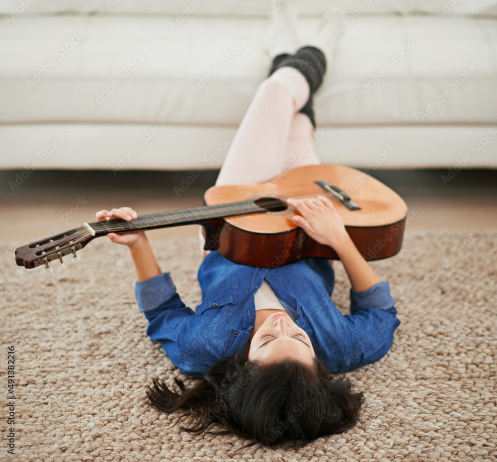 The perfect way to unwind. Shot of a young woman playing the guitar while lying on her living room f