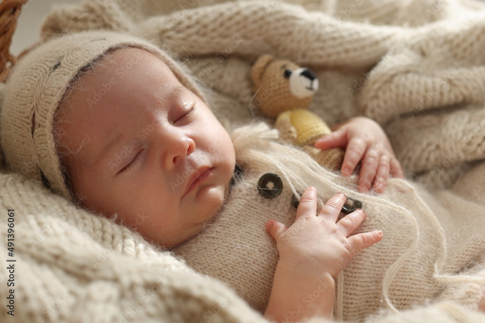 Adorable newborn baby with toy bear sleeping on knitted plaid, closeup