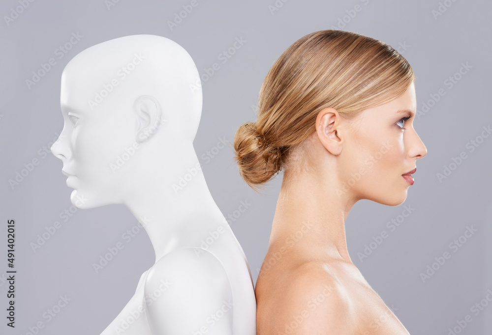 Real vs artificial beauty. A beautiful young woman standing back to back with a mannequin.