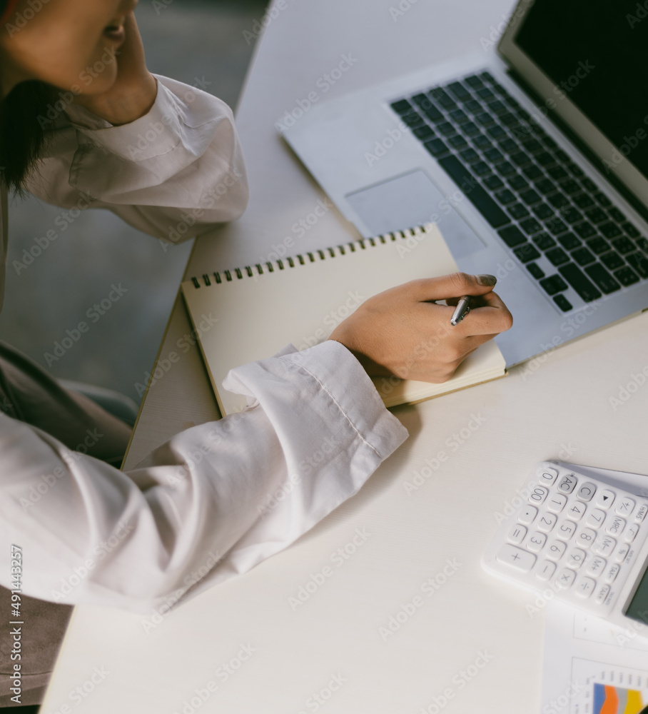 Woman working on laptop writing notes on notepad. Internet work from home and online learning concep