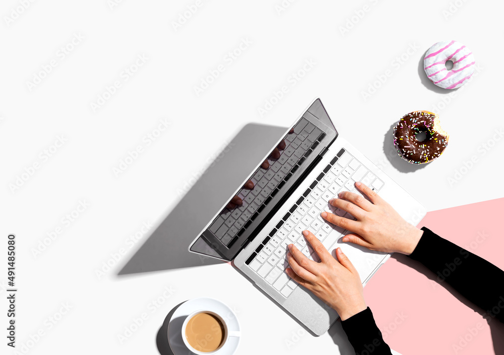 Person using a laptop computer with a donut and a cup of coffee - Flat lay