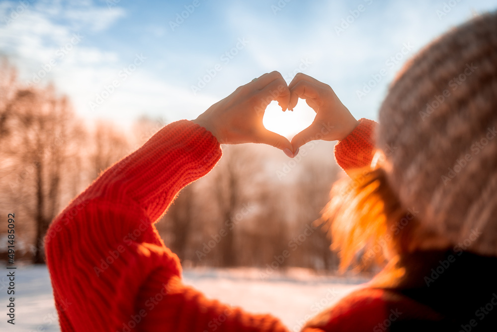 Love wintertime woman hands making heart shape during beautiful winter sunset