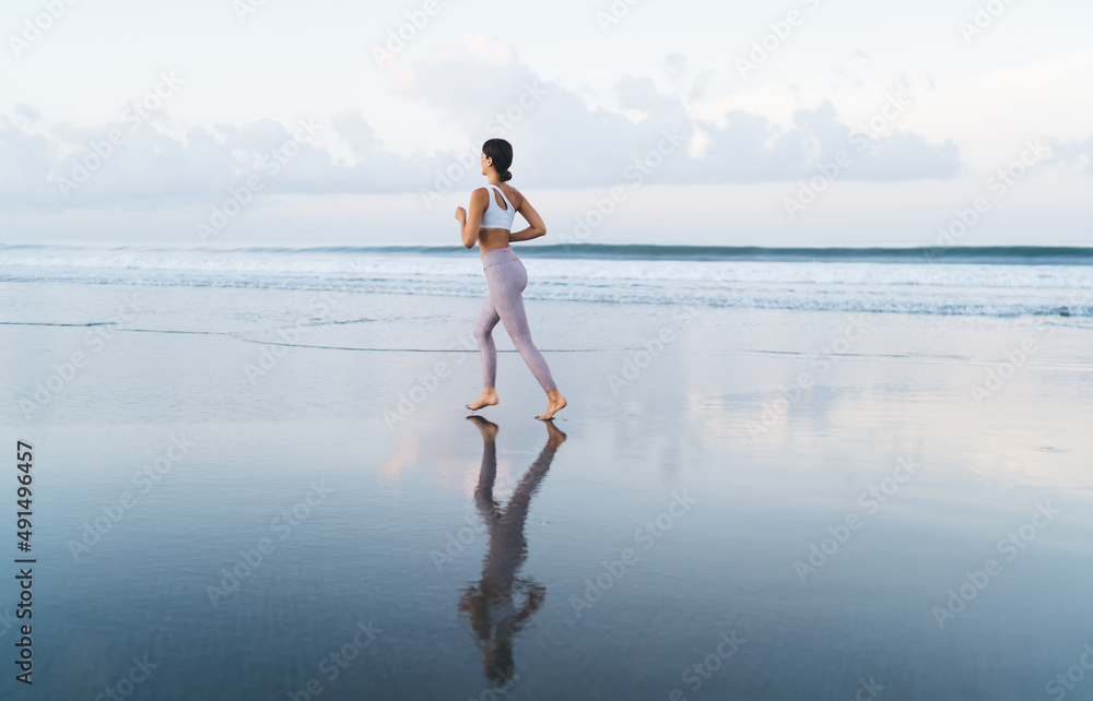 Active female in trendy sportswear enjoying time for morning jogging at seashore coastline, young Ca