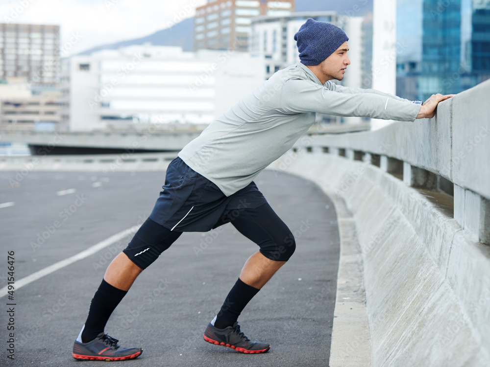 Getting ready for his run. Shot of a young man stretching before a jog through the quiet city street