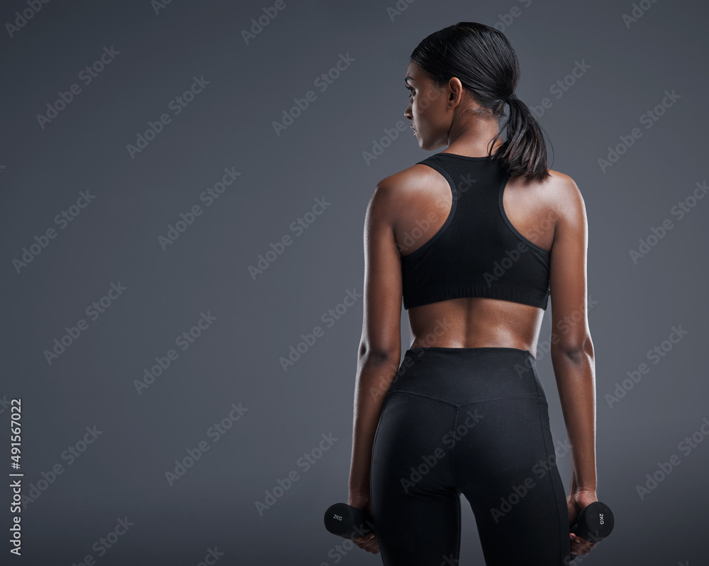 Every lift makes a difference. Studio shot of a sporty young woman lifting weights against a grey ba