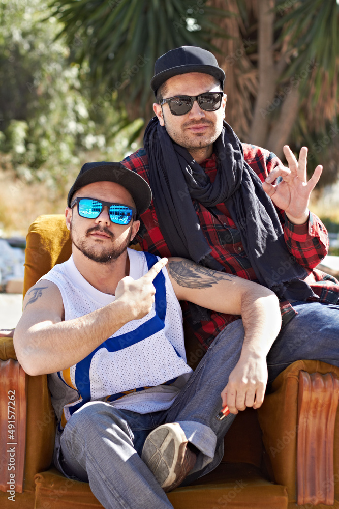 Confidence in our style. Two men sitting and posing in sunglasses in their neighborhood.