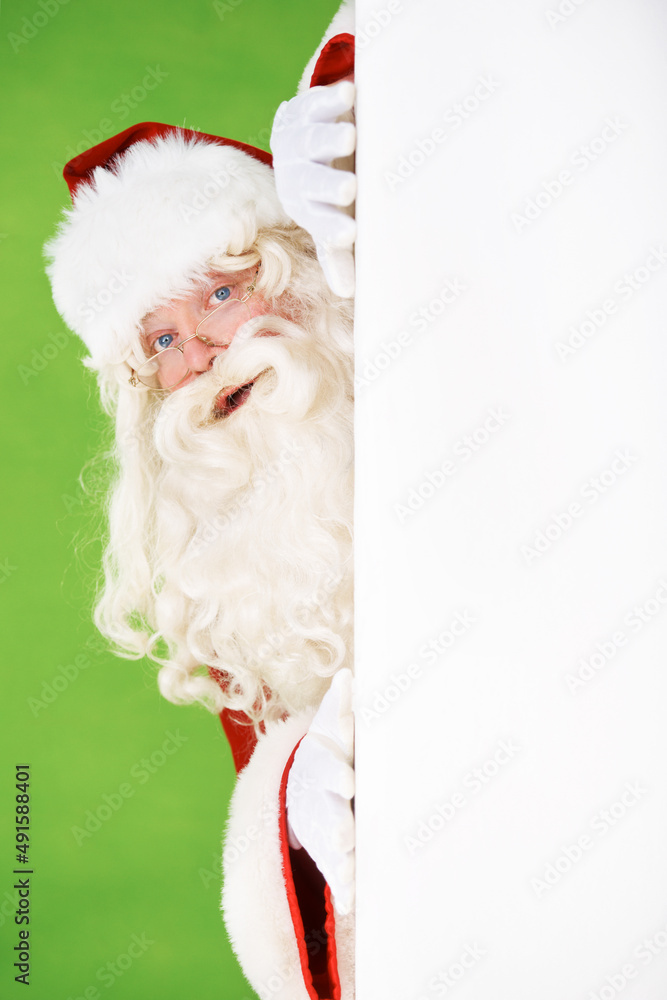 Peeping Santa. Santa peeking out around the corner of a white wall, on a green background - copyspac