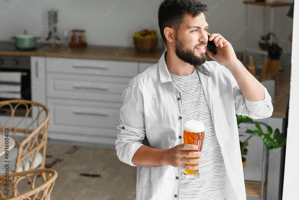 英俊的留着胡子的男人拿着一杯啤酒在厨房里用手机聊天