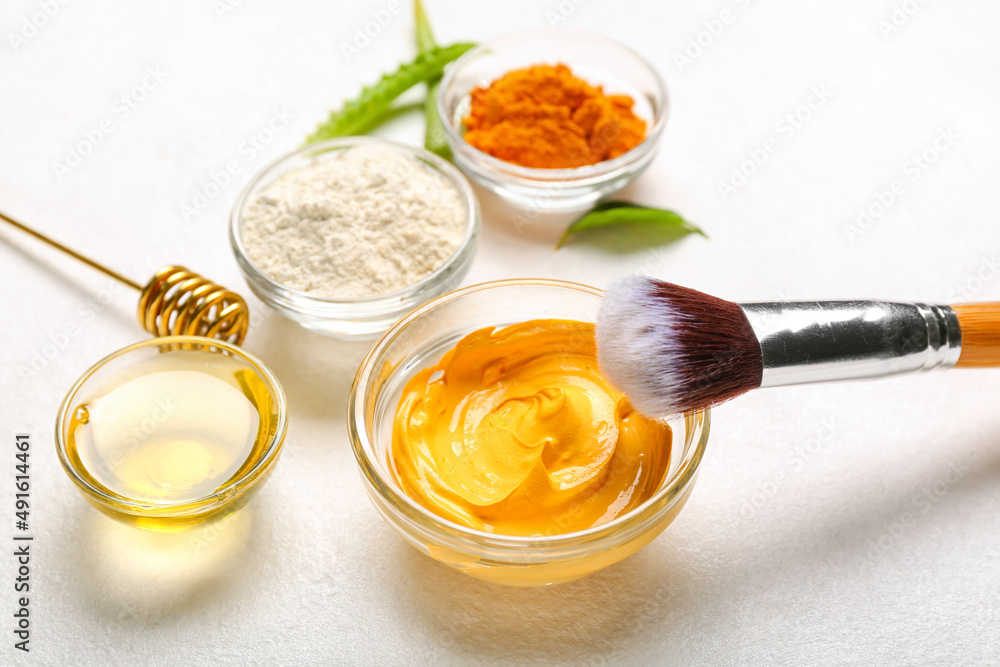 Bowl with turmeric mask and makeup brush on light background, closeup