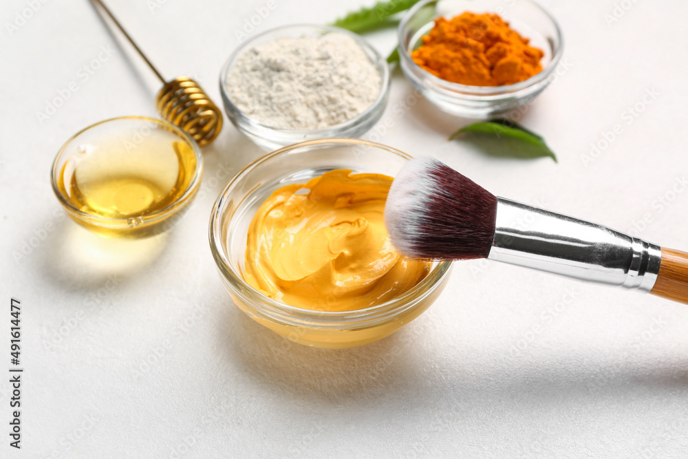 Bowl with turmeric mask and makeup brush on light background