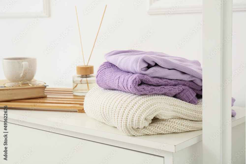 Knitted sweaters on shelf near light wall