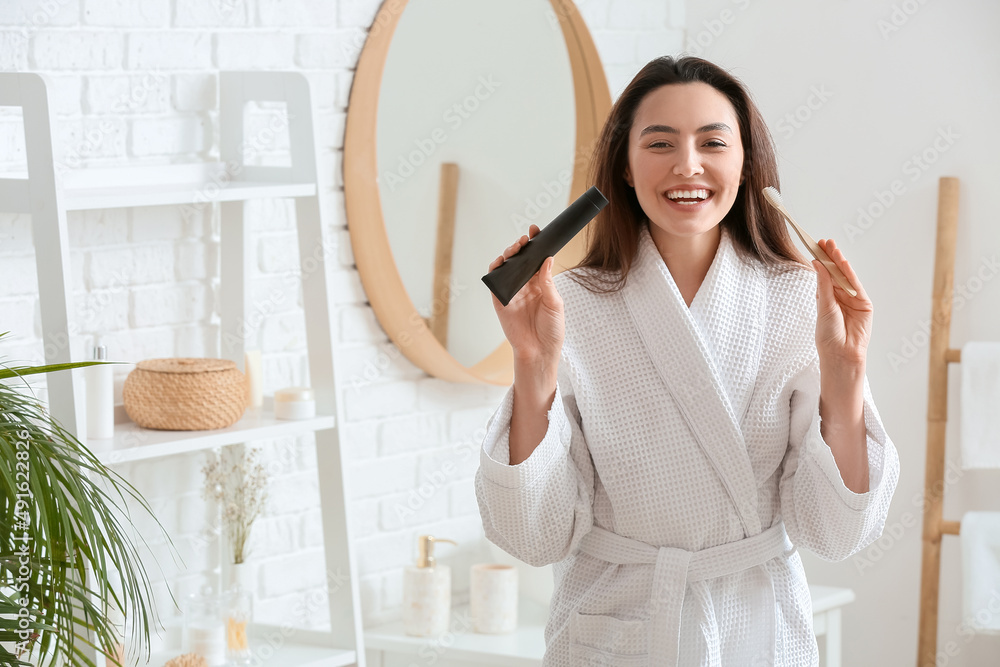 Beautiful young woman with activated charcoal tooth paste and brush in bathroom