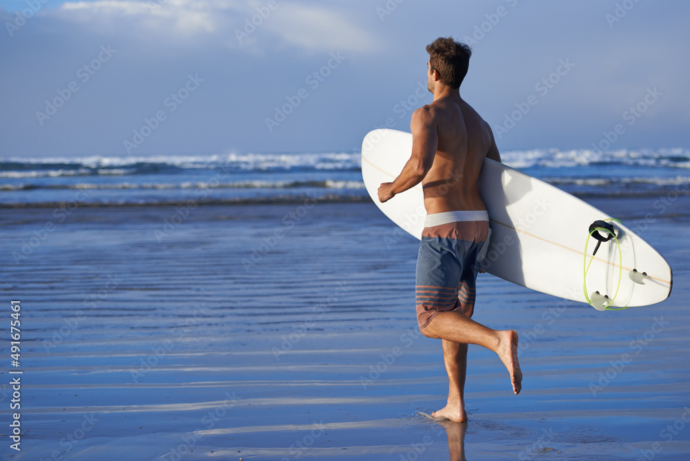 追逐海浪。一个英俊的年轻冲浪者在海滩上渴望一个好的海浪。