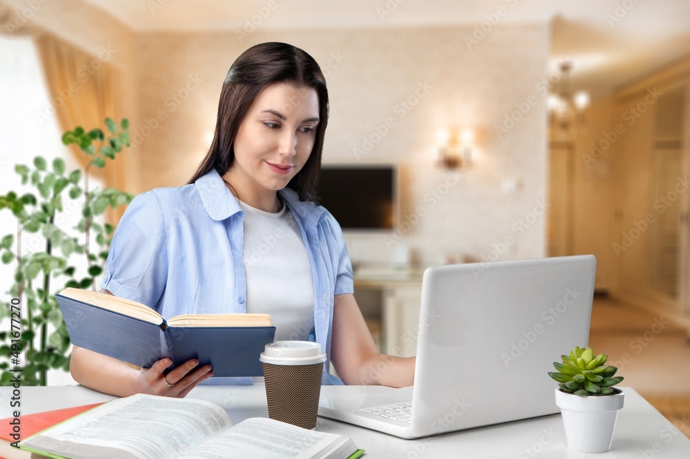 Young businesswoman studying online, watching podcast on laptop, making notes, sitting at work desk.