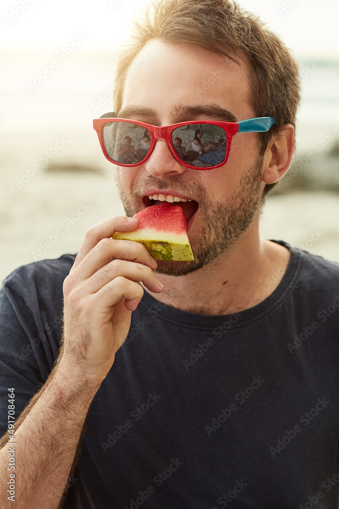 享受新鲜的水果美食。一个快乐的年轻人在海滩上吃西瓜的镜头。