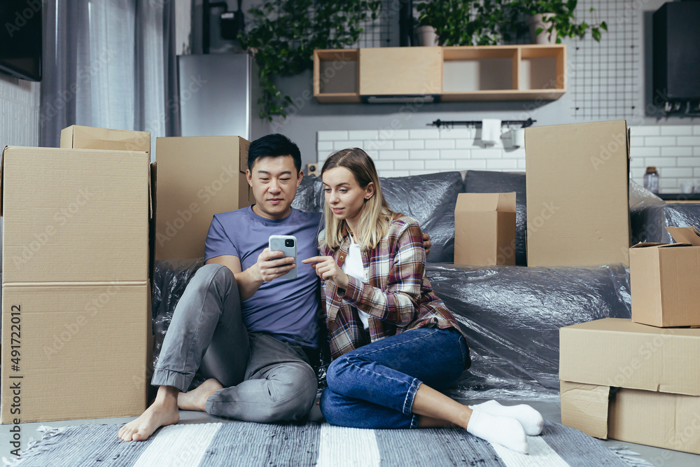 A young family in a new apartment among the cardboard boxes sitting on the floor and happily choosin