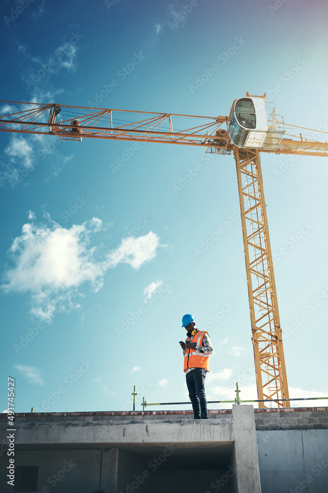 Updating project plans on the go. Shot of a young man using a smartphone while working at a construc