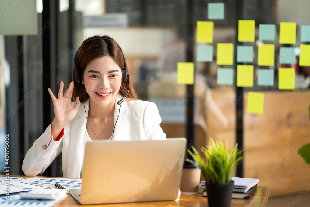 Confident young businesswoman wearing headphones and discussing project details with clients on vide