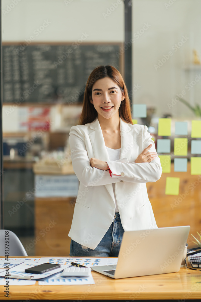 快乐的女高管双臂交叉站着。年轻的女商人站在办公室里。