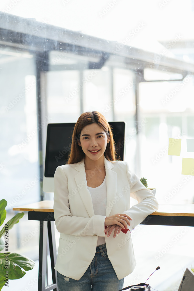 快乐的女高管双臂交叉站着。年轻的女商人站在办公室里。