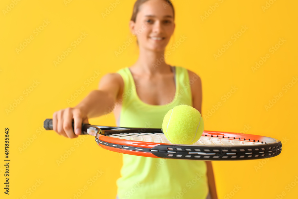 Sporty young woman with tennis racket and ball on yellow background, closeup