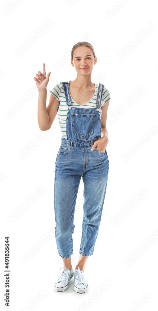 Young woman in denim jumpsuit pointing at something on white background