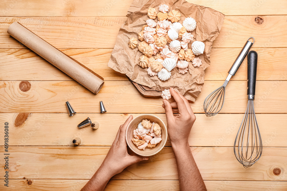 Female hands with sweet meringue and kitchen utensils on wooden background