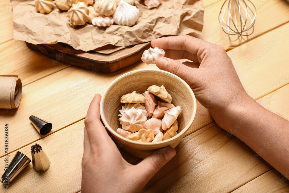 Woman holding bowl with tasty meringue on wooden background, closeup