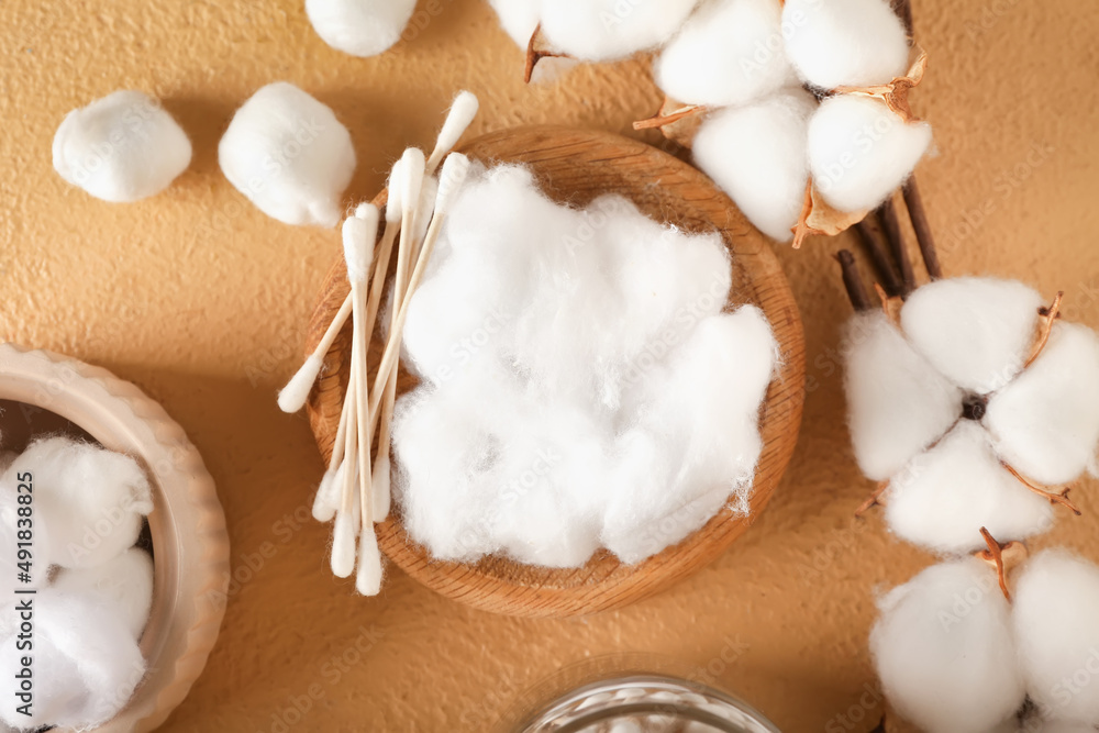 Bowl of cotton wool, swabs and flowers on color background, closeup