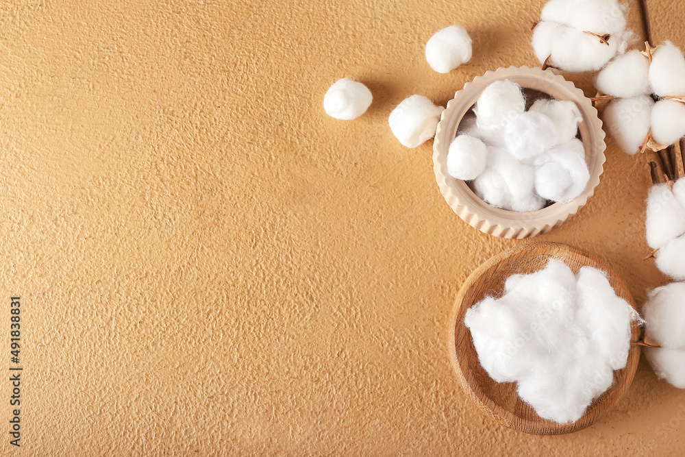 Bowls with cotton wool and balls on color background