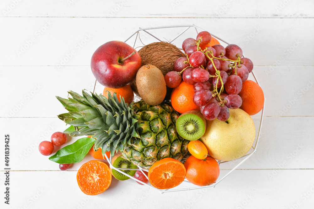 Basket with juicy fruits on white wooden background