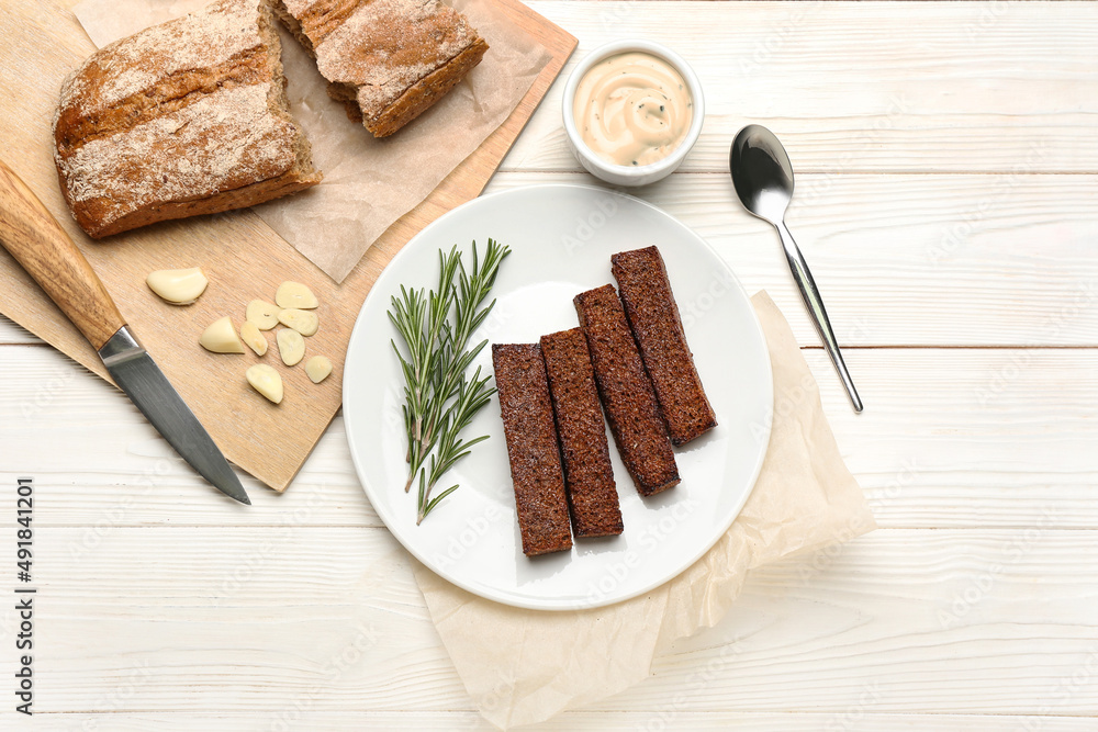 Plate with tasty croutons, sauce and bread on white wooden background