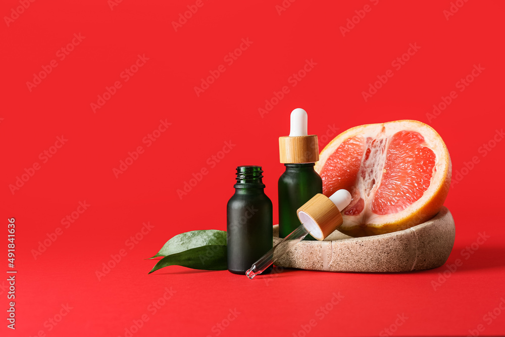 Composition with bottles of essential oil and juicy grapefruit on red background