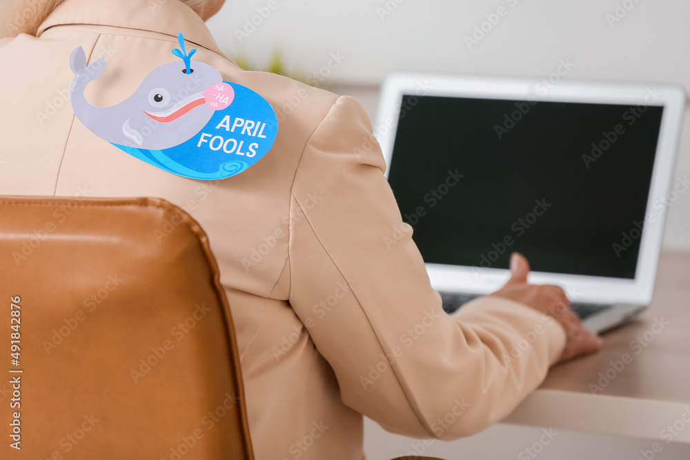 Mature woman with paper whale attached to her back in office. April fools day celebration