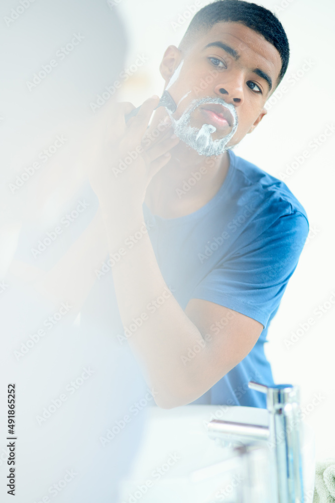 Time to shave this all off. Shot of young man shaving his face in his bathroom mirror.