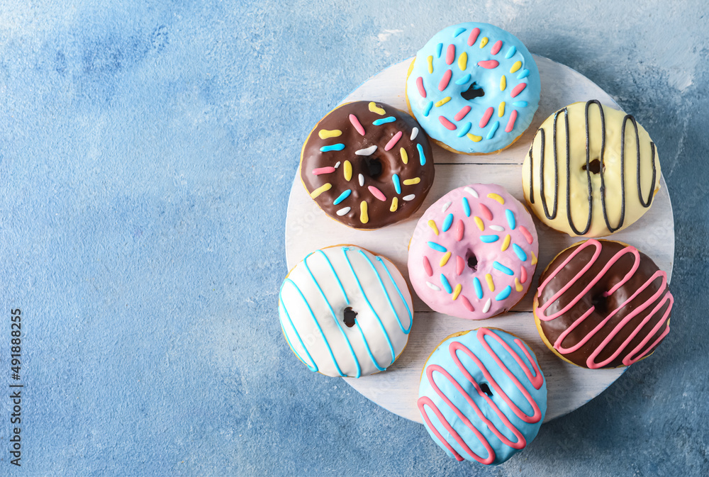 Board with different delicious donuts on color background