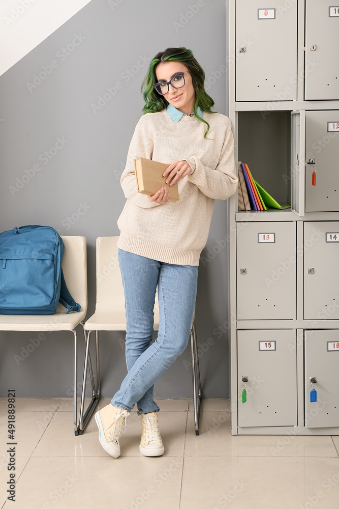 Beautiful female student with book near locker at the university