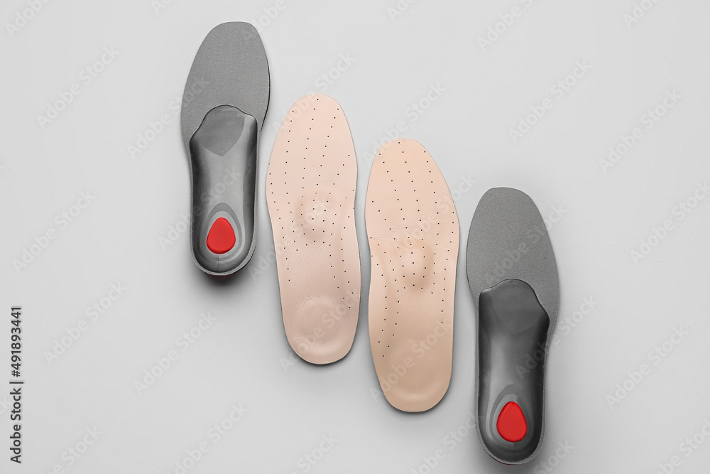 Two pairs of orthopedic insoles on grey background