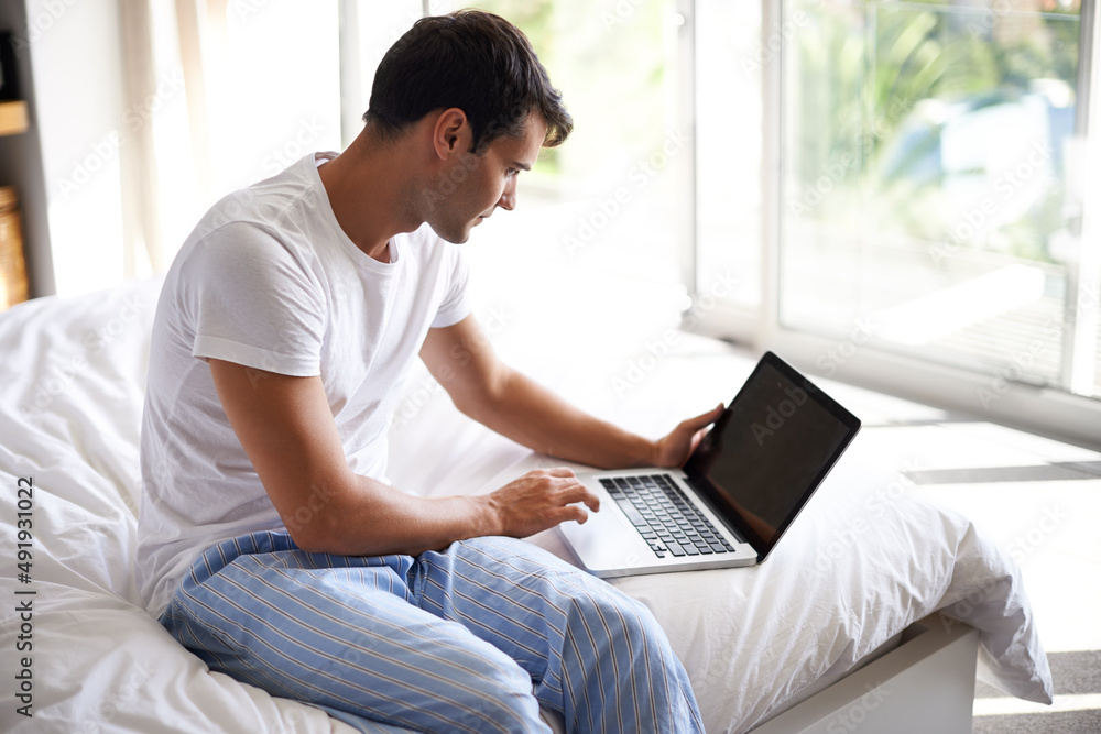 Checking his emails in the morning. Cropped shot of a handsome young man using a laptop on the edge 