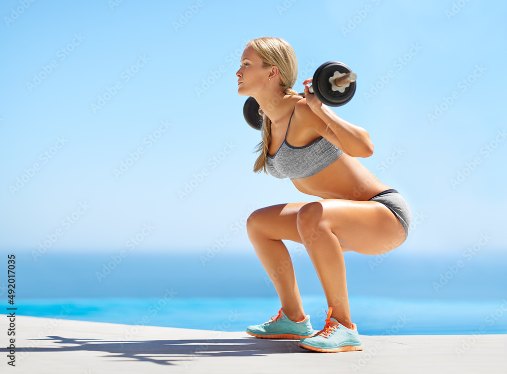 Lift with your legs. Full length shot of an attractive young woman doing squats with a barbell outsi