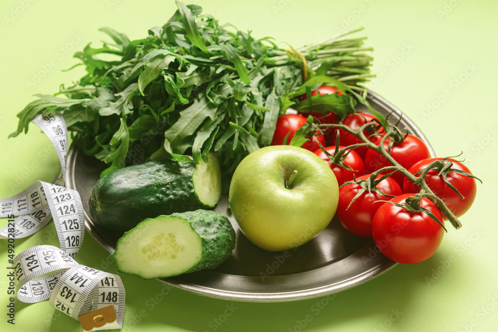 Plate with healthy products and measuring tape on green background, closeup