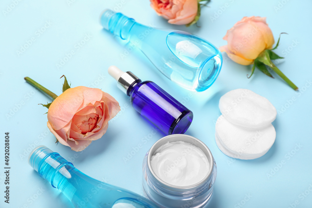 Cosmetic products, cotton pads and rose flowers on color background, closeup