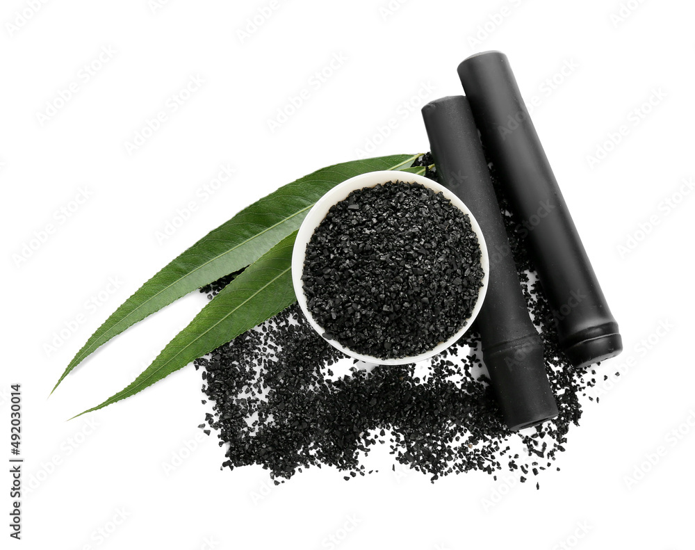 Bowl with activated carbon powder and black bamboo sticks on white background